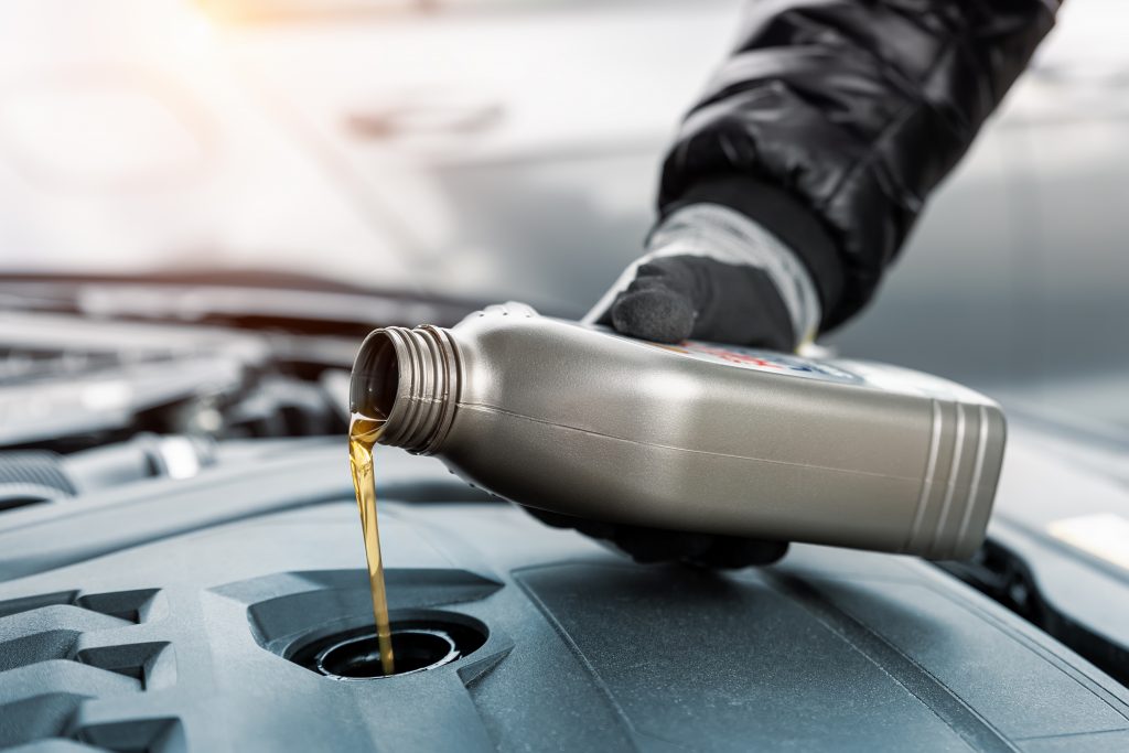 close up driver hand holding small bottle can pouring synthetic motor oil in diesel or petrol turbocharged vehicle engine due oil consumption. new lubricant diy change. car service maintenance work