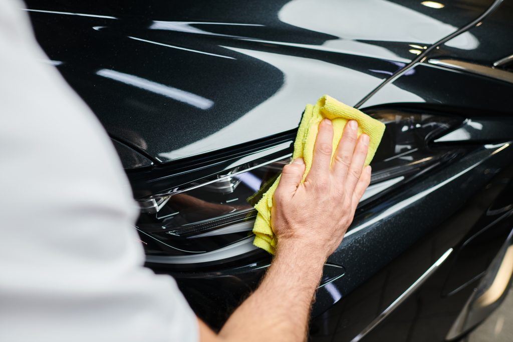 cropped view of hard working professional serviceman cleaning car with rag while in garage